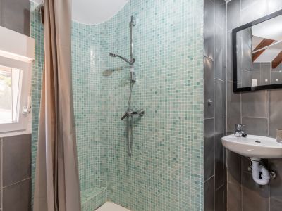 Badkamerdetail met turquoise mozaïekdouche, hangend wastafel en grijze betegelde muren.