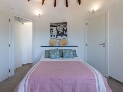 Lichte slaapkamer met tweepersoonsbed, roze beddengoed en een hoofdeinde versierd met waaiers.
