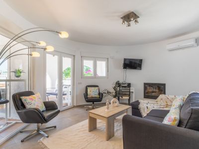 Lichte woonkamer met donkergrijze bank, leren fauteuils en ingebouwde open haard.