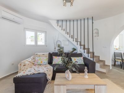 Lichte woonkamer met grijze bank, stenen trap met zwarte leuning en lichte houten salontafel.