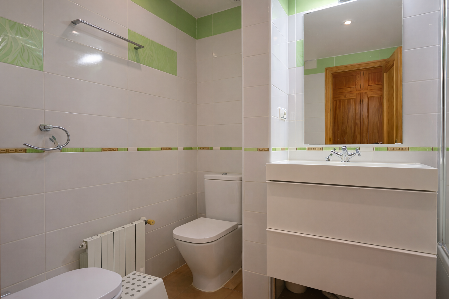 Badkamer met witte tegels, groene accenten, modern wastafelmeubel en spiegel.