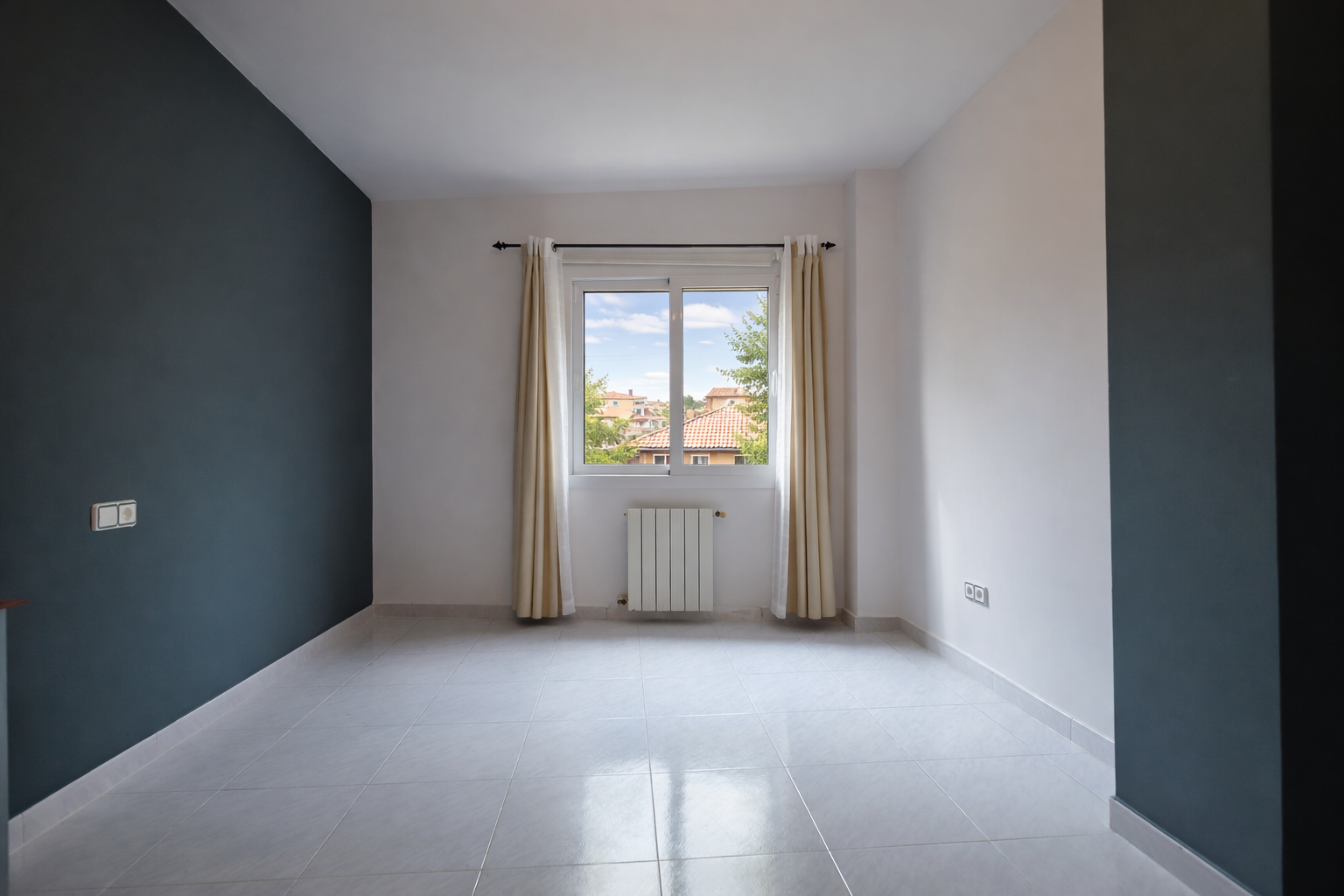 Lichte kamer met loodblauwe accentmuur, raam met uitzicht en tegelvloer.