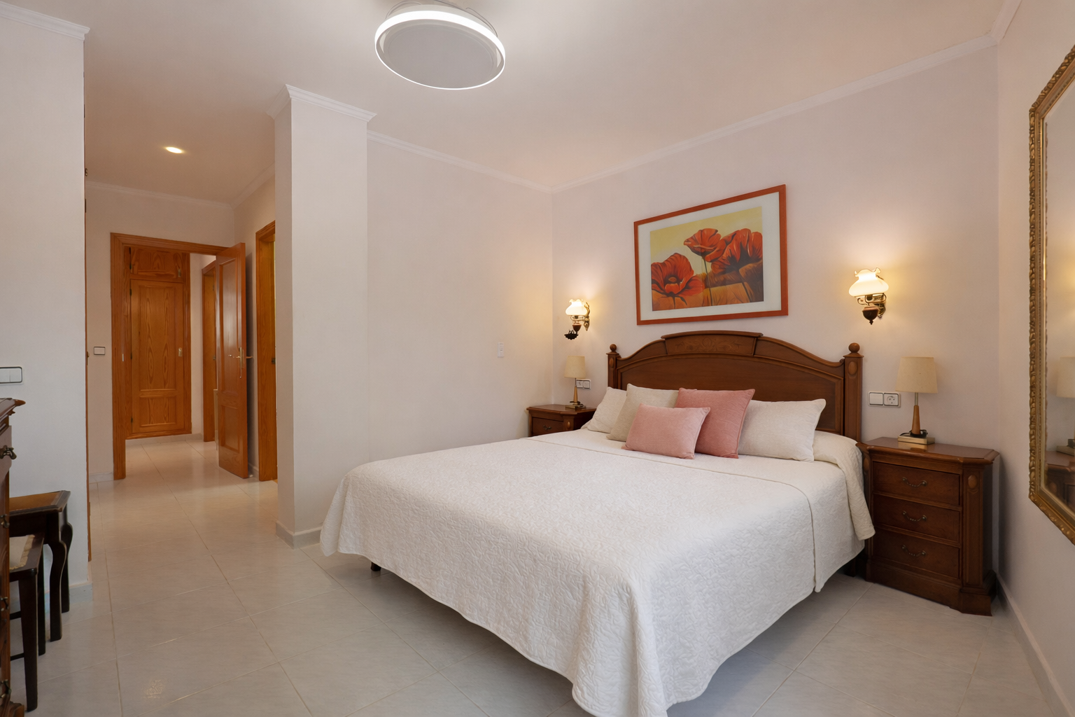 Lichte slaapkamer met tweepersoonsbed, houten nachtkastjes en tegelvloer.