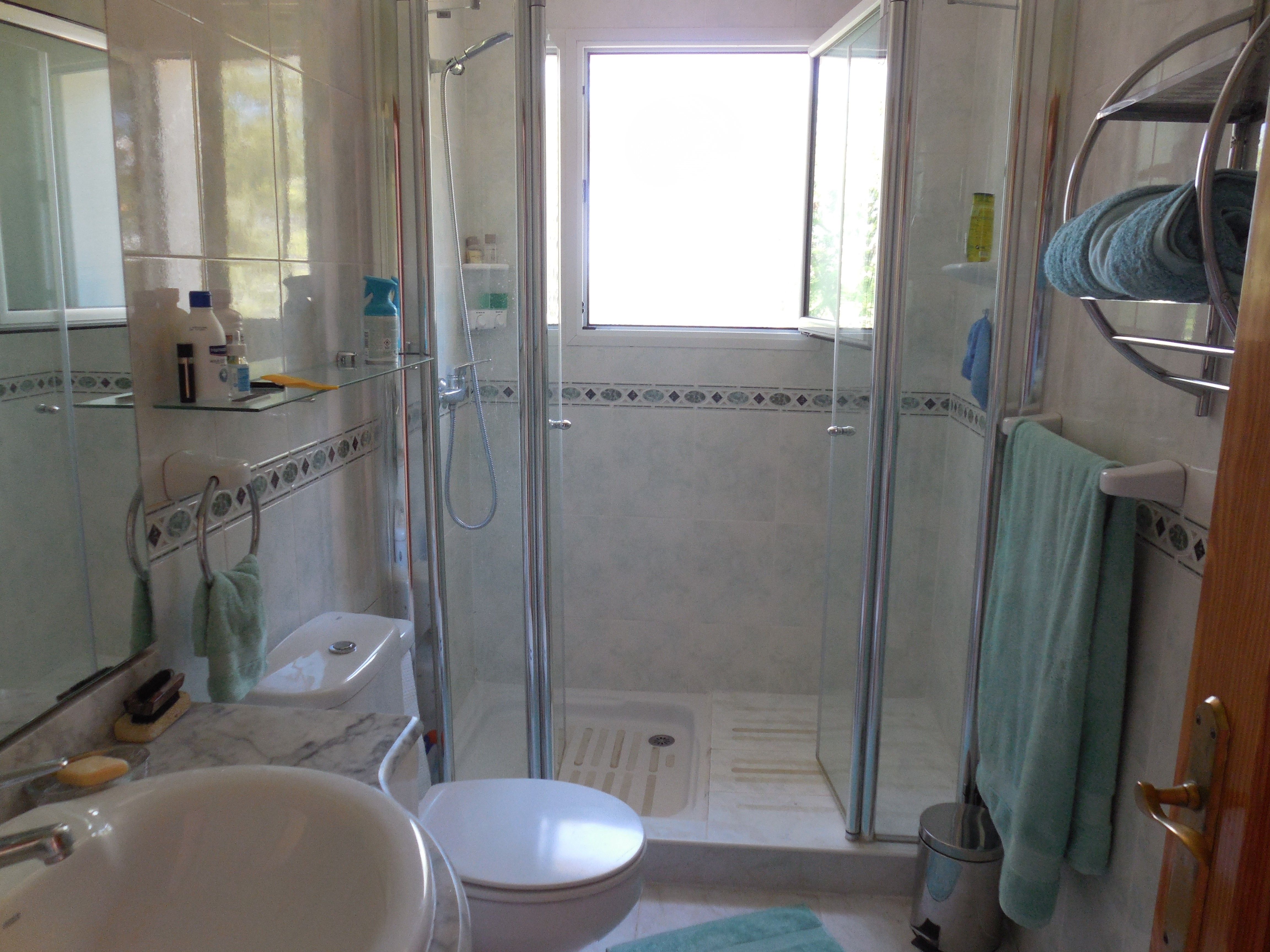 Badkamer met glazen douchecabine, wastafel met marmeren blad en decoratieve tegels.