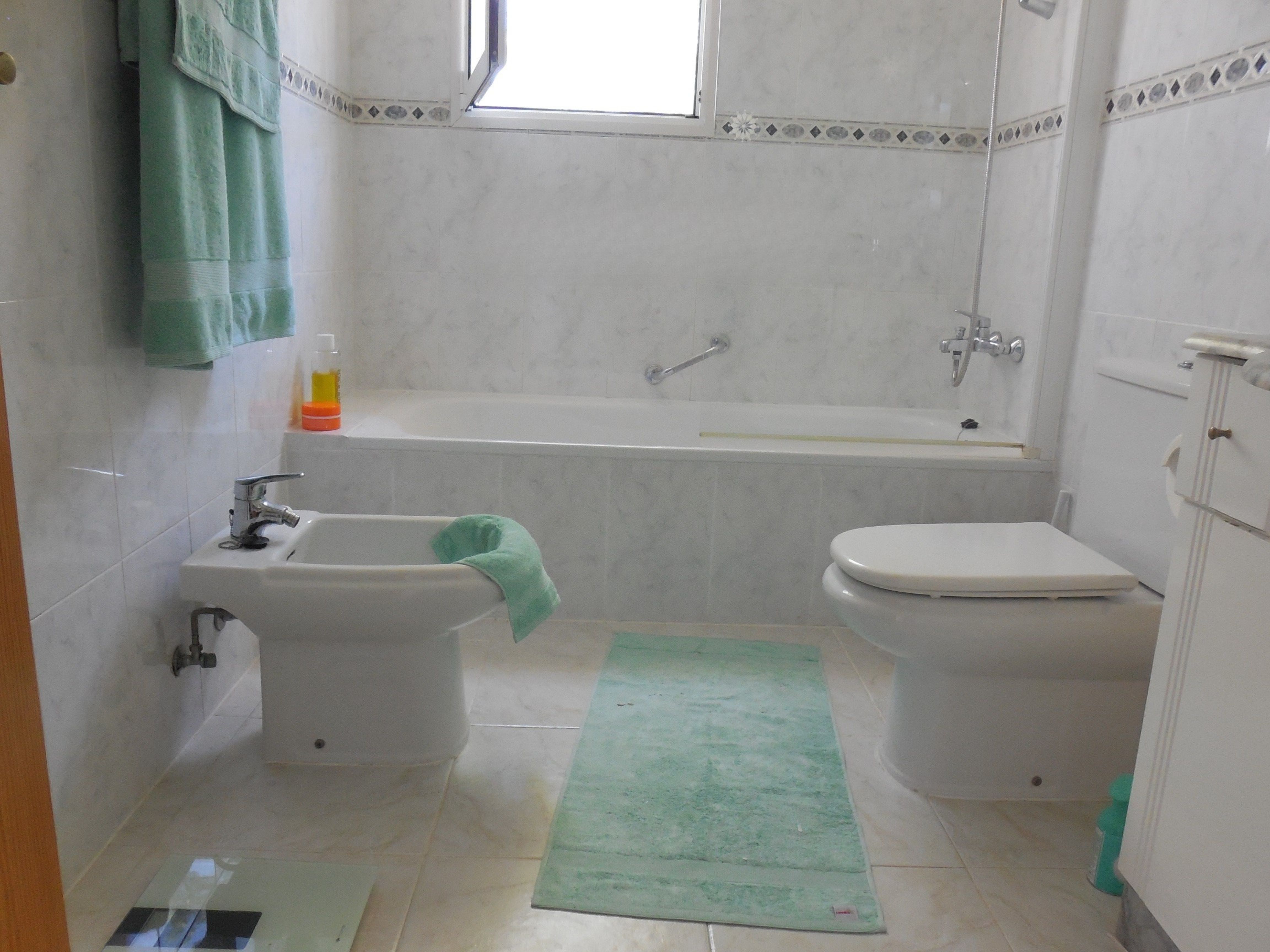 Badkamer met marmerachtige tegels, een bad, bidet en mintgroene handdoeken.