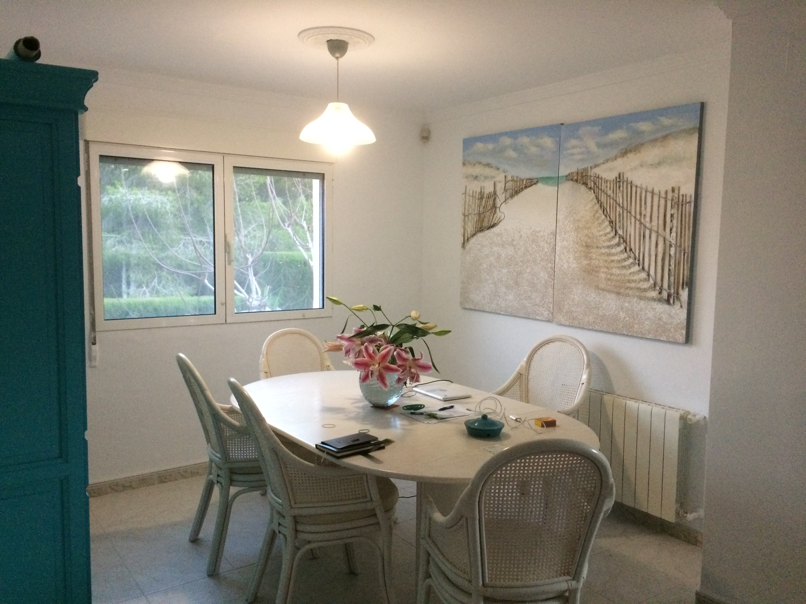 Lichte eetkamer met ovale stenen tafel, rieten stoelen en een schilderij met een strandthema.