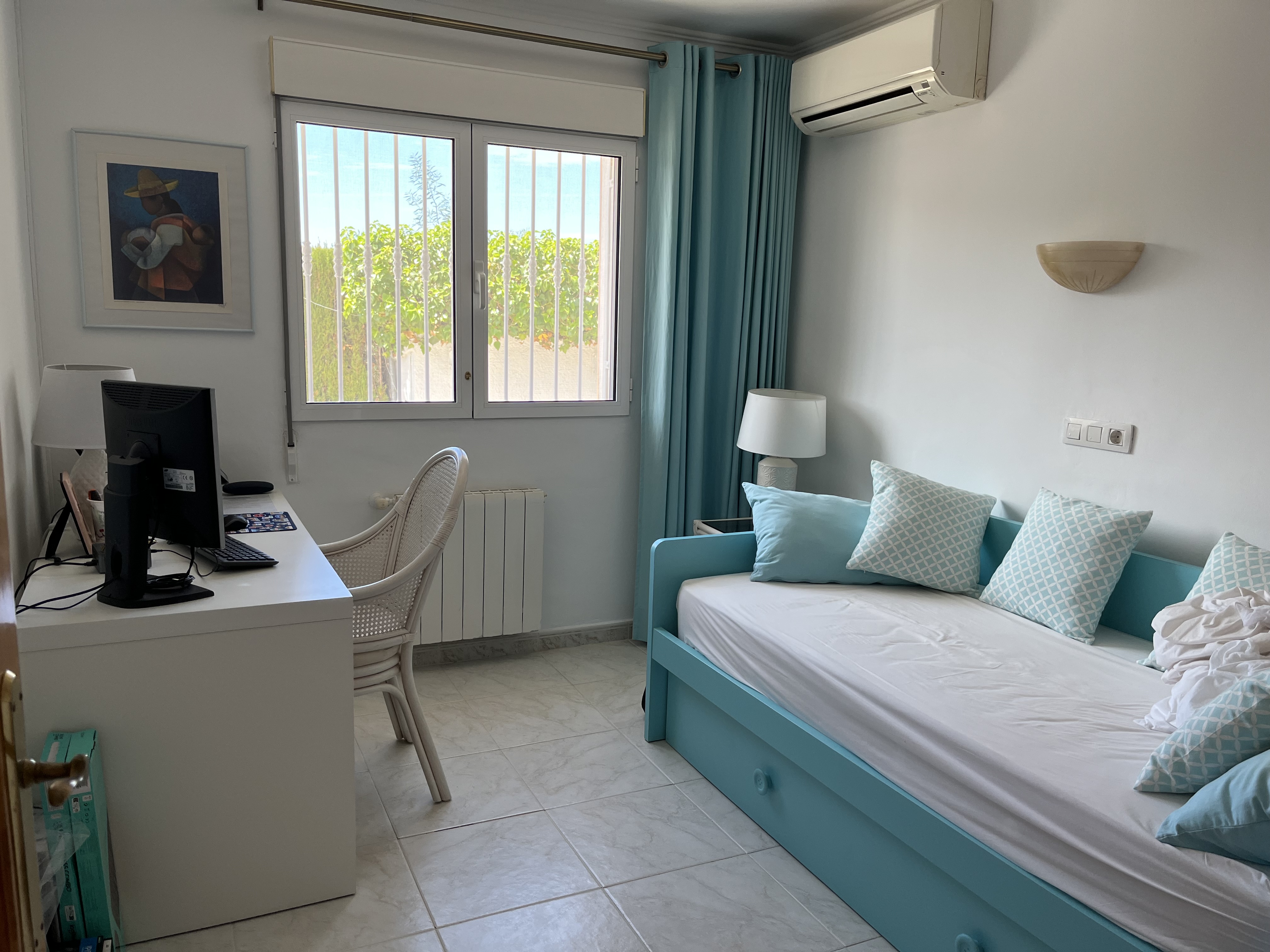 Lichte slaapkamer met turquoise bedbank, wit bureau en uitzicht op de tuin.