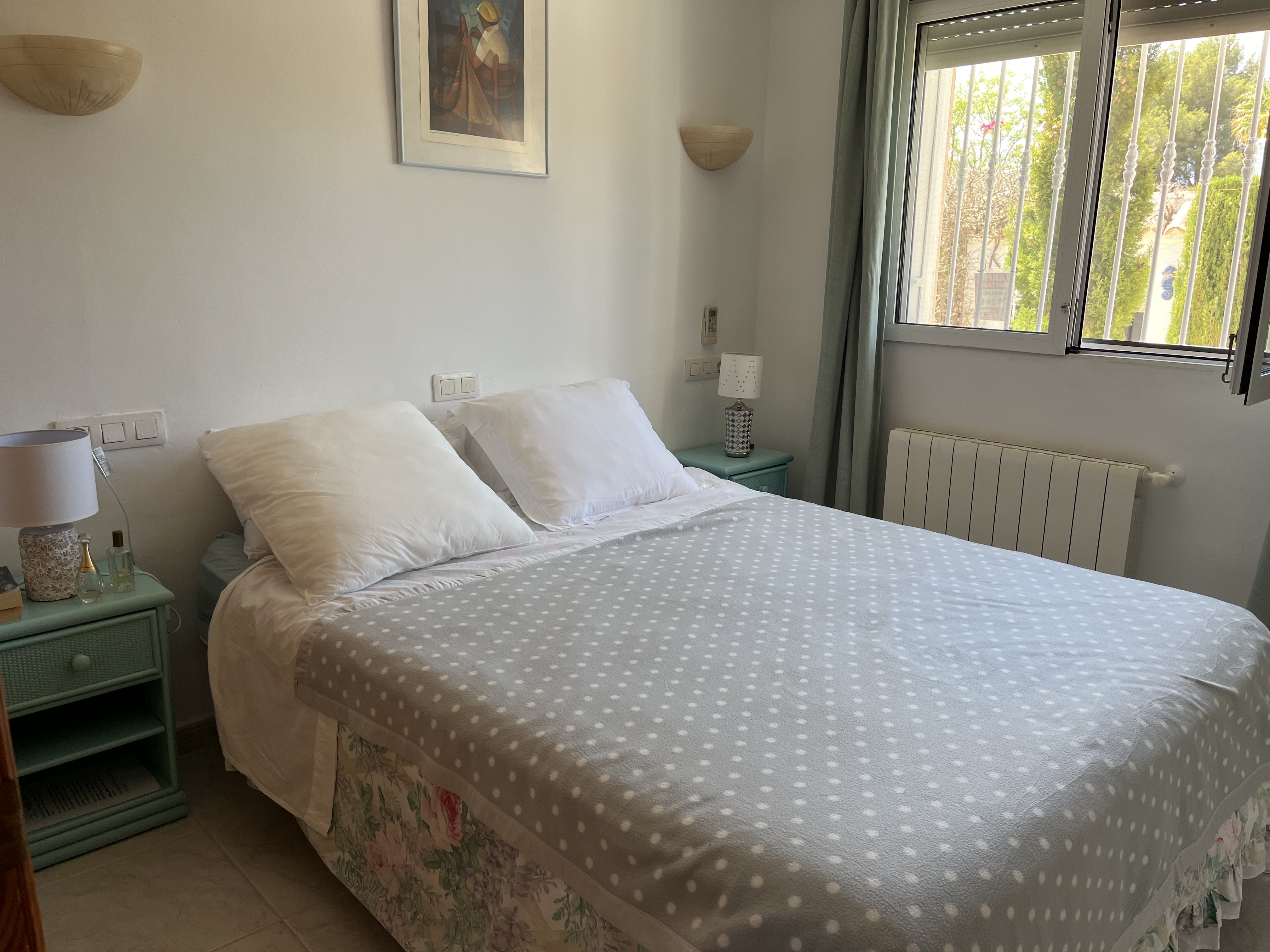 Lichte slaapkamer met tweepersoonsbed, turquoise nachtkastje en decoratieve details.