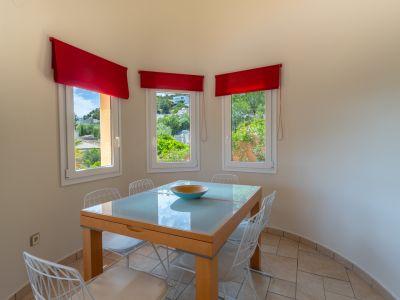 Lichte eetkamer met glazen tafel en uitzicht door ramen met rode gordijnen.