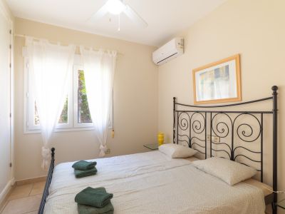 Lichte slaapkamer met twee eenpersoonsbedden, een smeedijzeren hoofdeinde en uitzicht naar buiten door witte gordijnen.