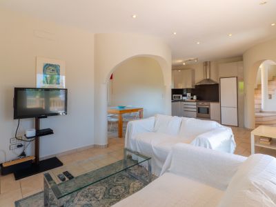 Lichte woonkamer met bogen die verbinding maken met de keuken en eetkamer. Witte bank met hoes en glazen salontafel.