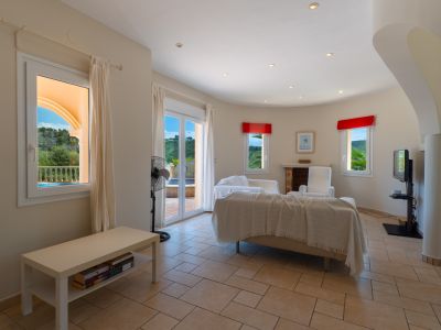Lichte woonkamer met tegelvloer, een beige bank met een sprei en uitzicht naar buiten.