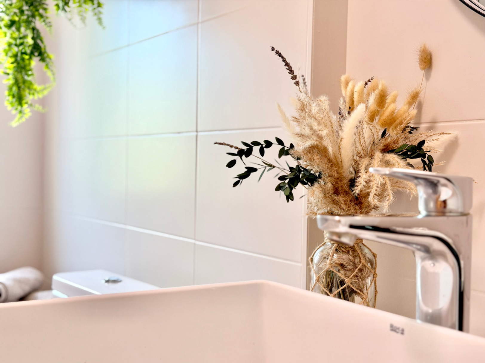 Badkamerdetail met witte wastafel, moderne kraan en minimalistische bloemdecoratie.
