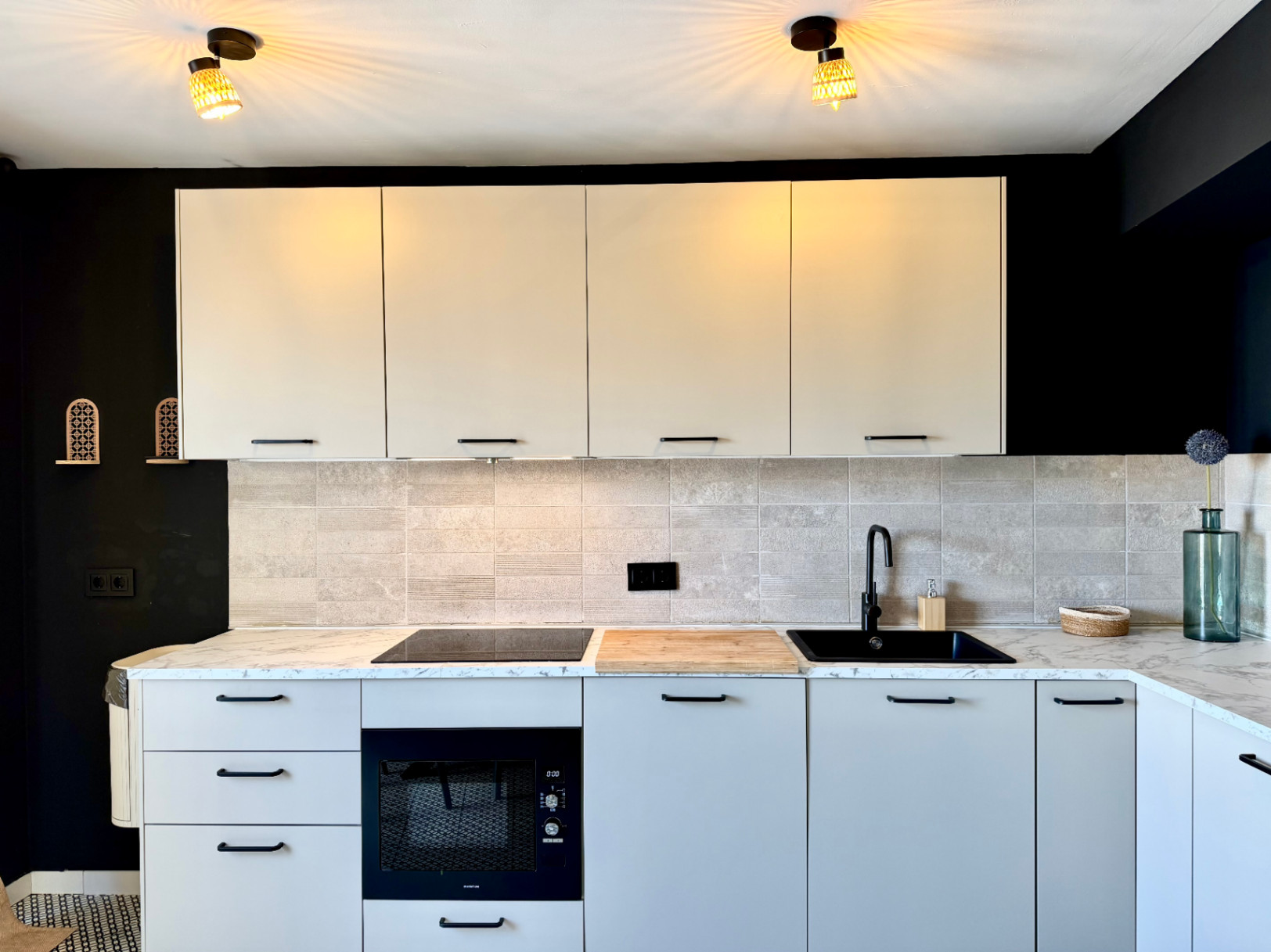 Close-up van de gerenoveerde keuken met een marmeren aanrechtblad, lichte kasten en een contrasterende zwarte muur.