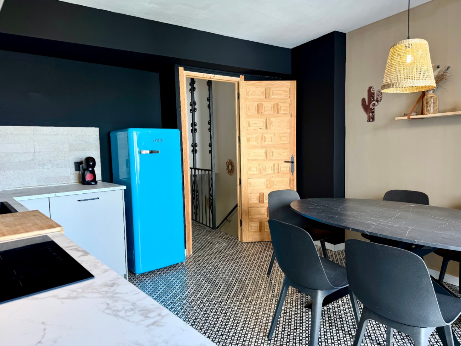 Keukendetail met retro blauwe koelkast, ovale eettafel en gesneden houten deur.