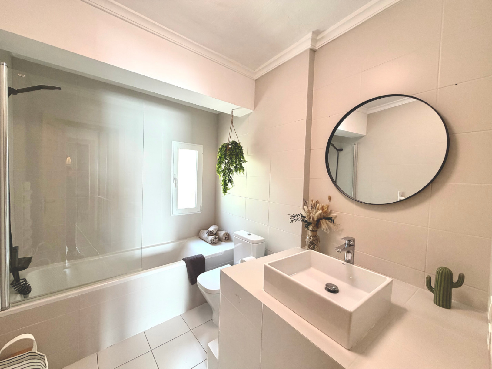 Lichte badkamer met ligbad, moderne wastafel en ronde spiegel. Minimalistische inrichting met natuurlijke accenten.