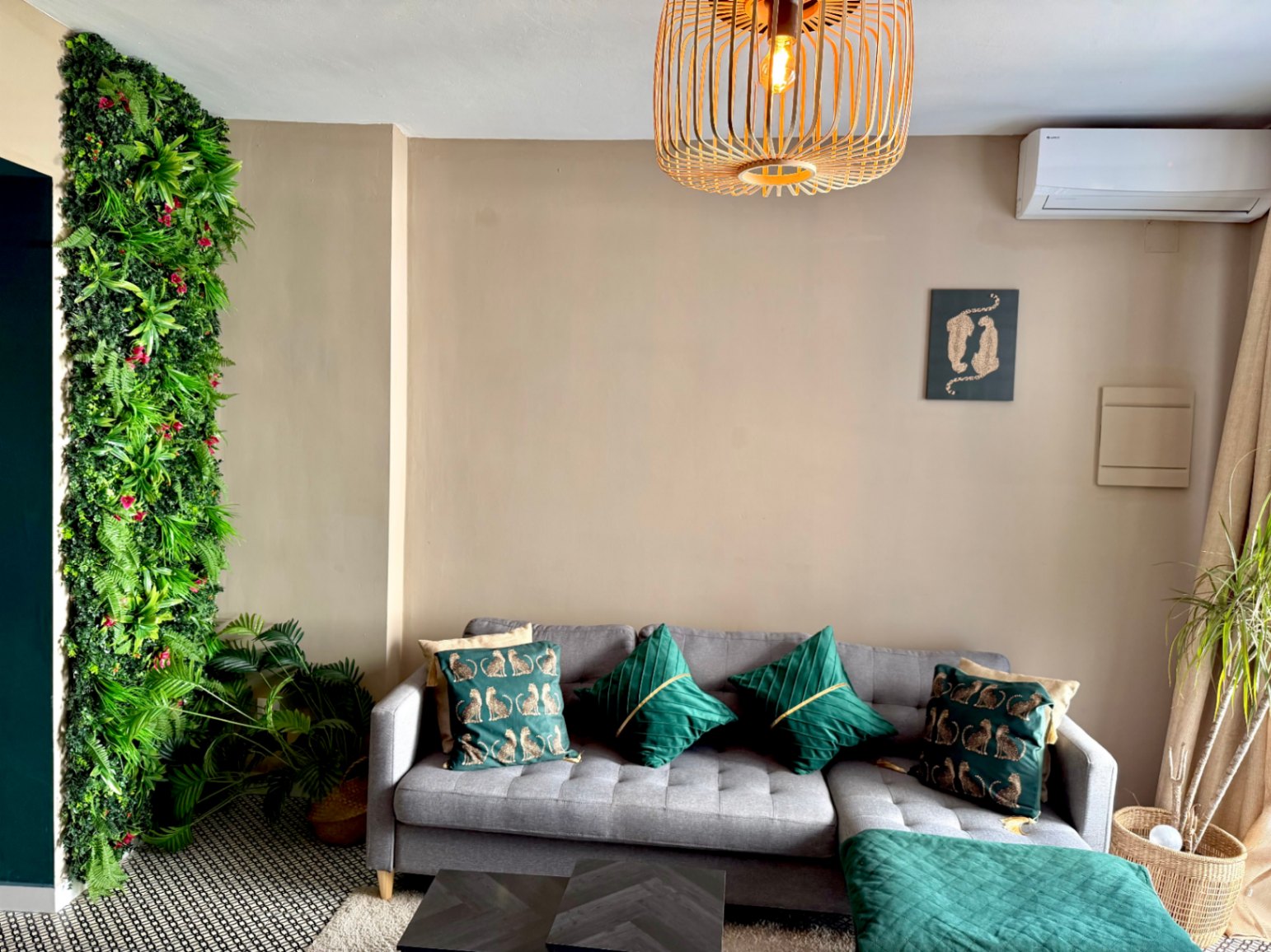 Lichte woonkamer met een verticale groene wand, grijze bank met decoratieve kussens en een donkere salontafel.