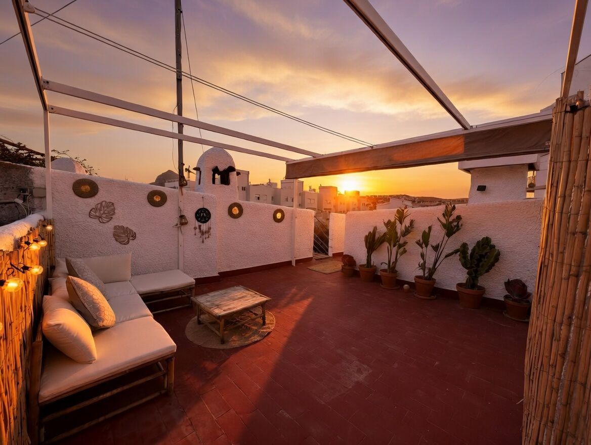 Privé terras met terracotta tegels, potplanten en bamboe meubilair bij zonsondergang.