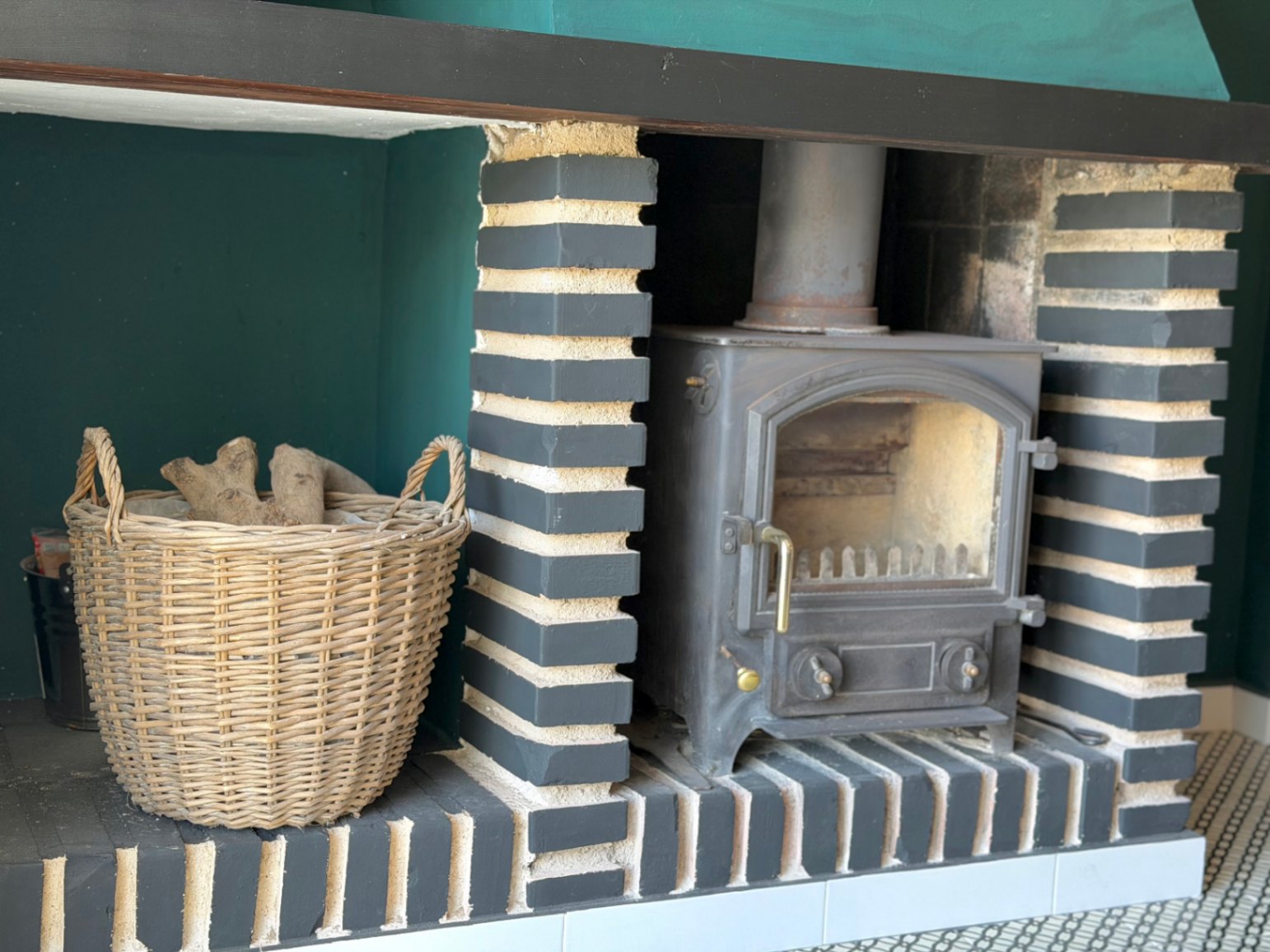 Rustieke open haard met geschilderde baksteendetails en een geweven houten mand van wicker.