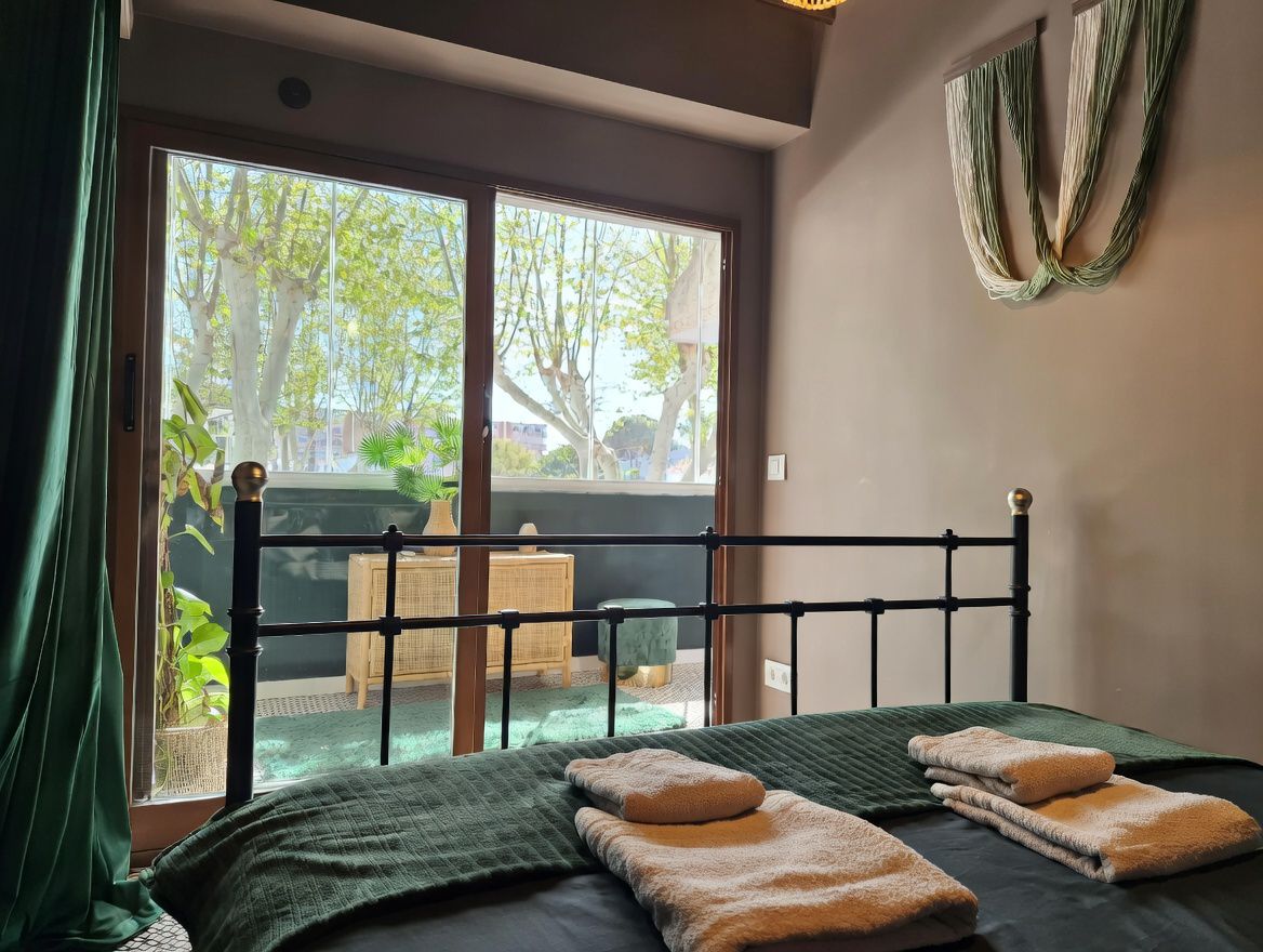 Slaapkamer met smeedijzeren bed en terras met uitzicht op bomen. Minimalistische inrichting in neutrale en groene tinten.
