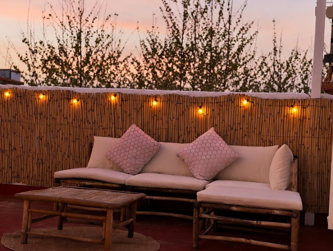 Terras met bamboe bank en kussens met patroon, verlicht met warme lichtjes, met uitzicht op de zonsondergang.