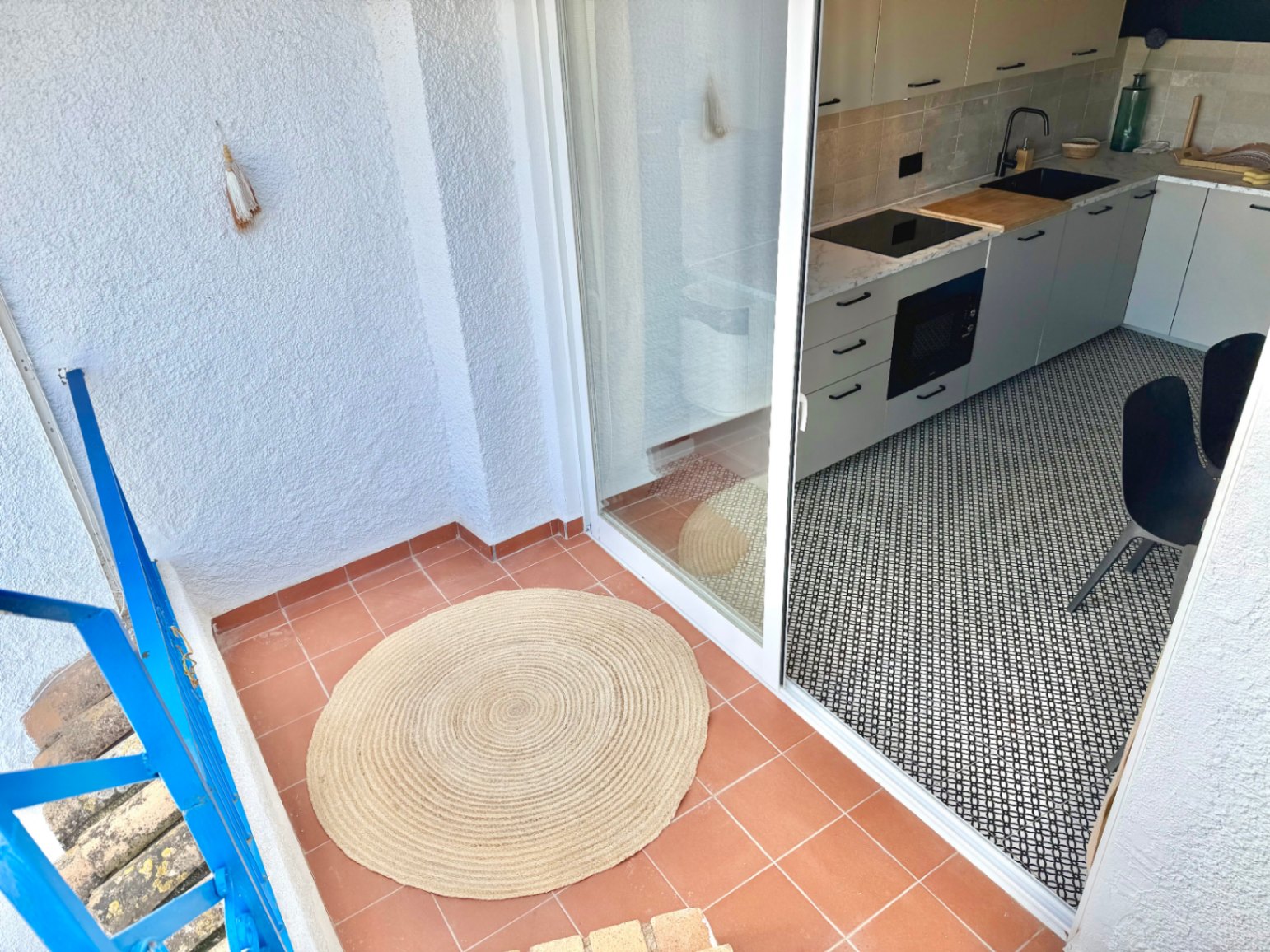 Terras met terracotta vloer en toegang tot een moderne keuken met zwart-wit geometrische vloer.