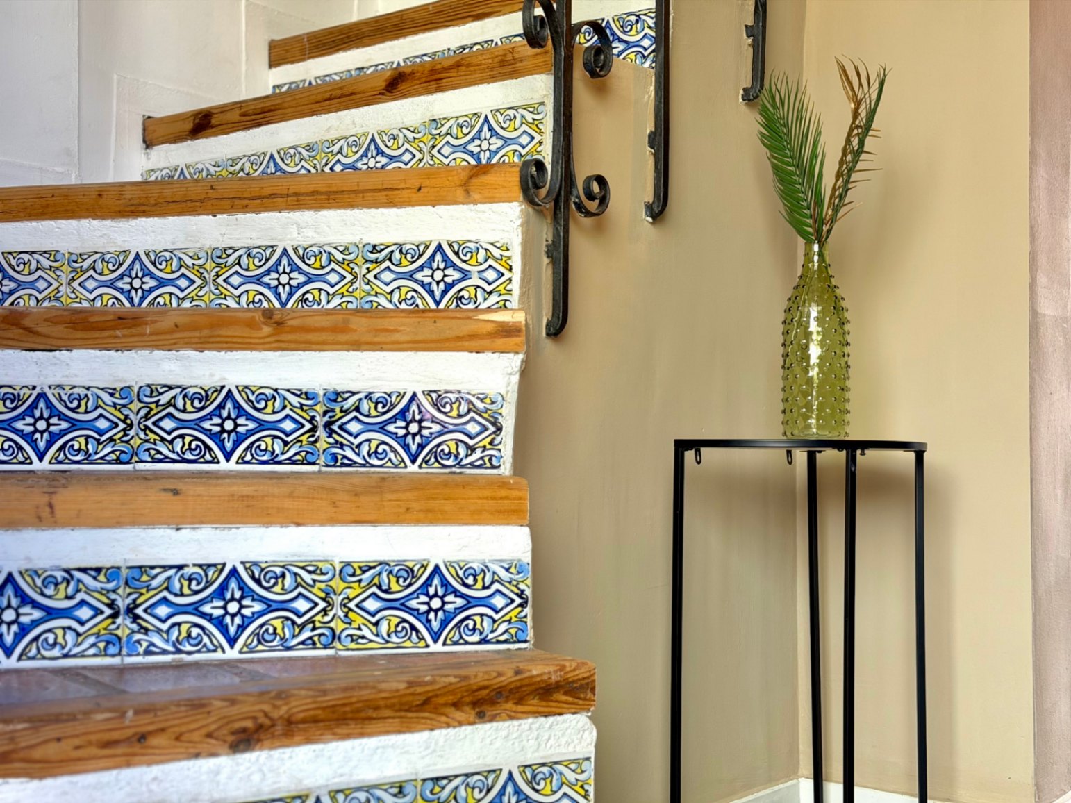 Trapdetail met decoratieve tegels en smeedijzeren leuning. Groene vaas met plant.