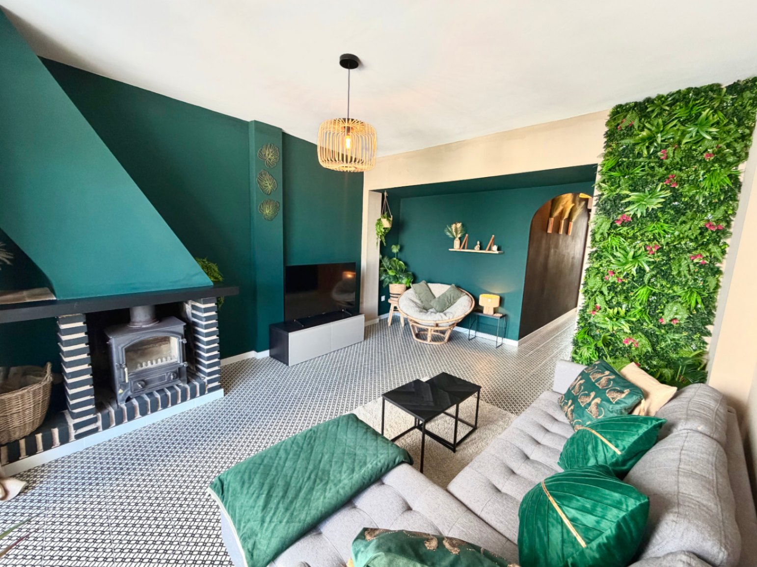 Woonkamer met open haard, verticale groene wand en zwart-witte geometrische vloer.