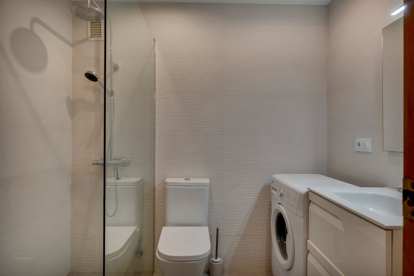 Badkamer met glazen douche, wit toilet, wasmachine en wastafelmeubel met witte kast.