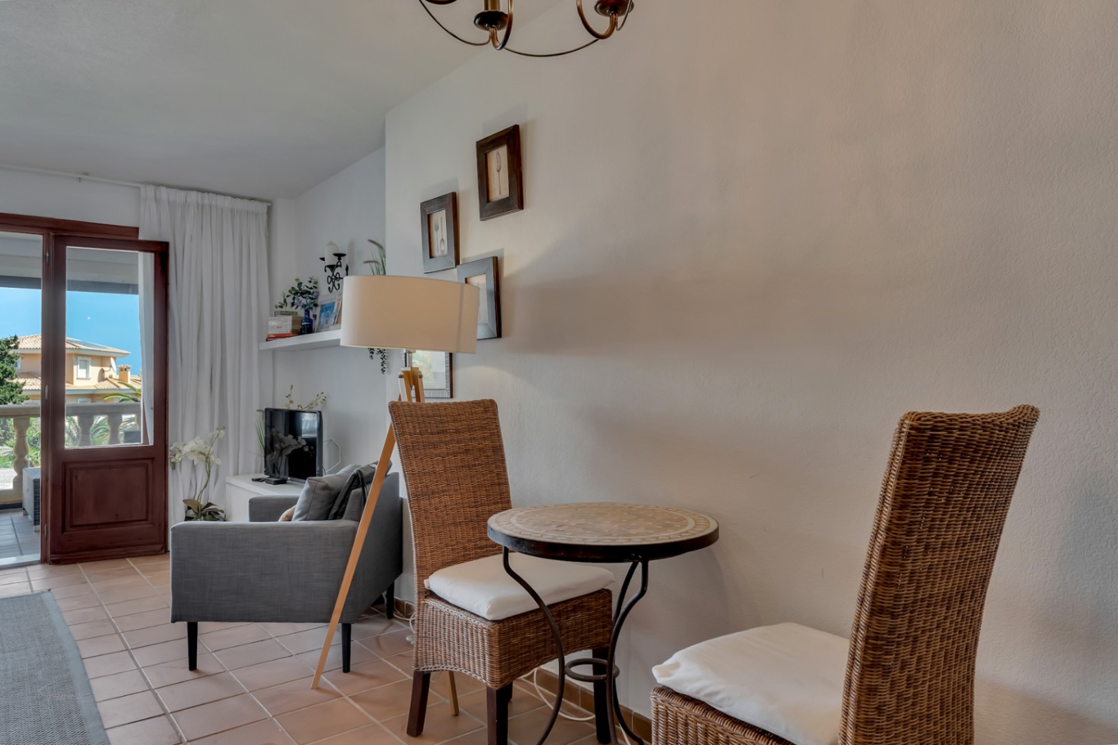 Gezellige hoek met mozaïektafel en rieten stoelen, verlicht door een vloerlamp en natuurlijk licht van het terras.