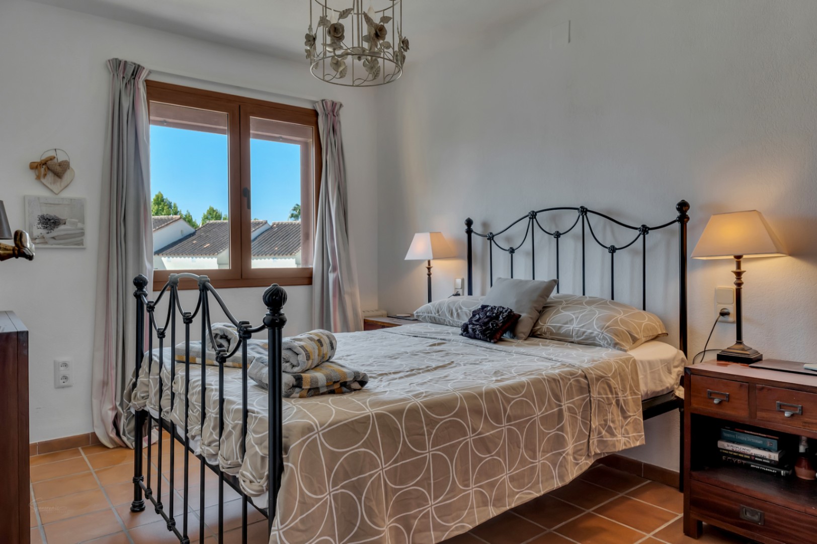Lichte slaapkamer met smeedijzeren bed, uitzicht vanuit het raam en terracotta vloertegels.
