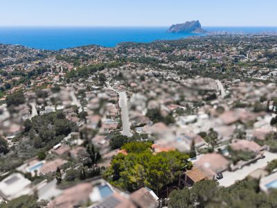 Luchtfoto van een residentiële kuststreek met de Middellandse Zee en de Peñón de Ifach in de verte, onder een helderblauwe hemel.