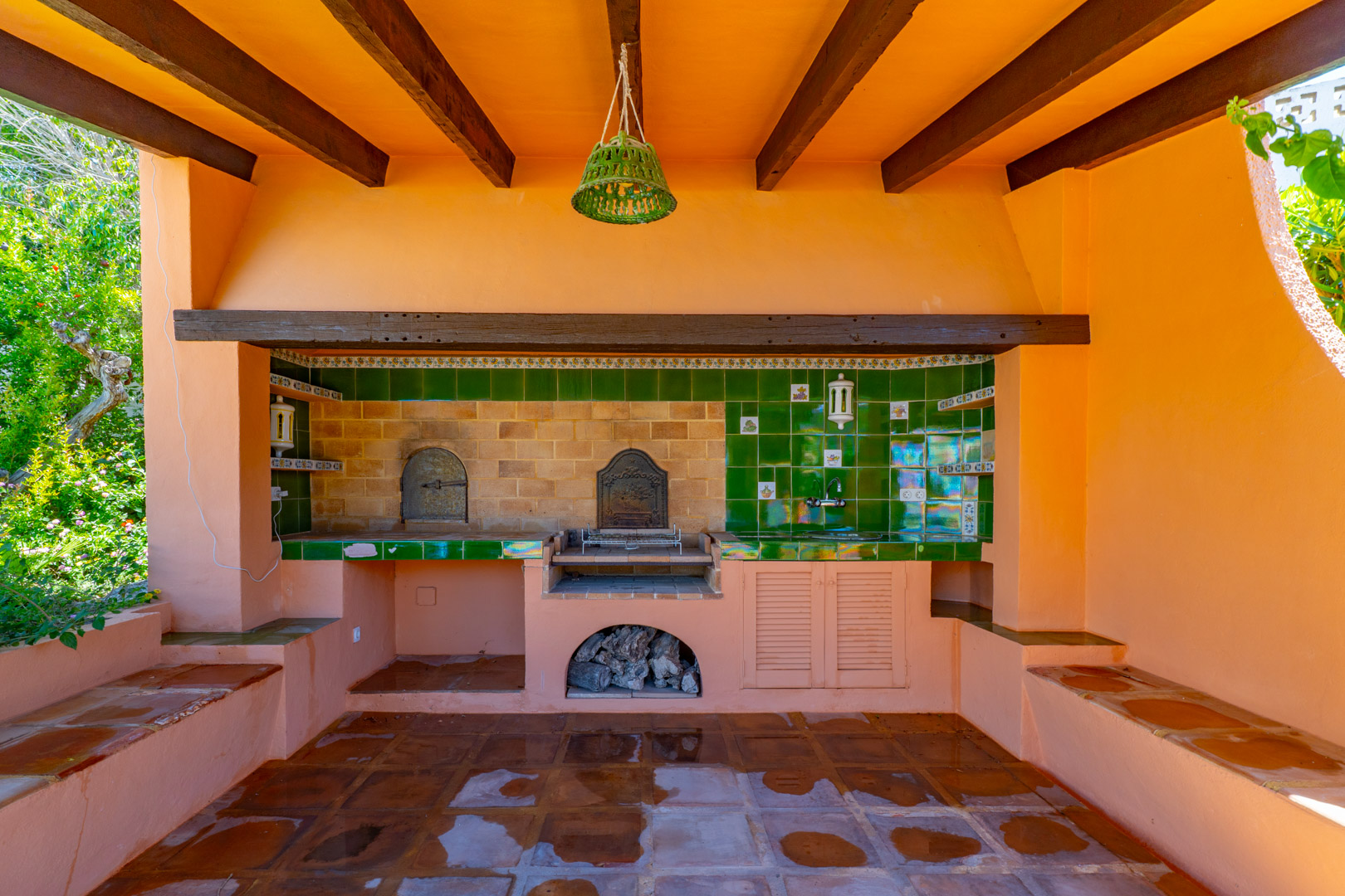 Buiten barbecue met houtoven, spoelbak en terracotta vloertegels.