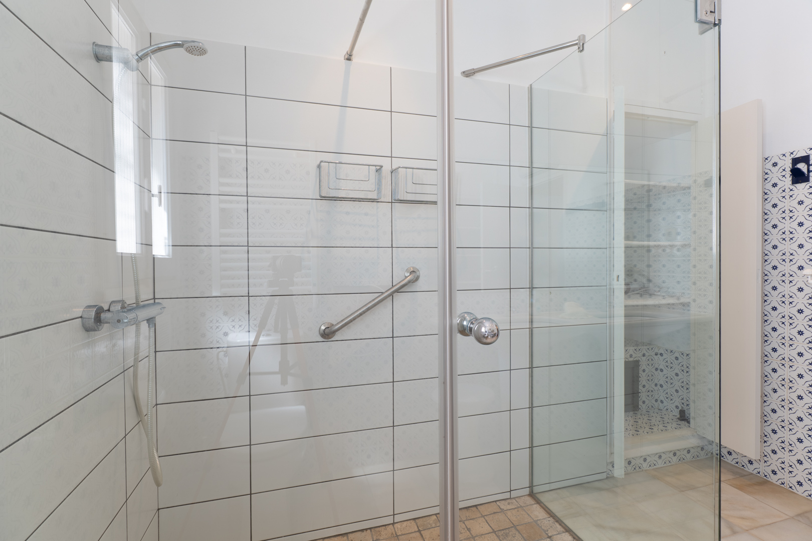 Close-up van de douche met glazen wand en witte tegels met subtiele patronen.