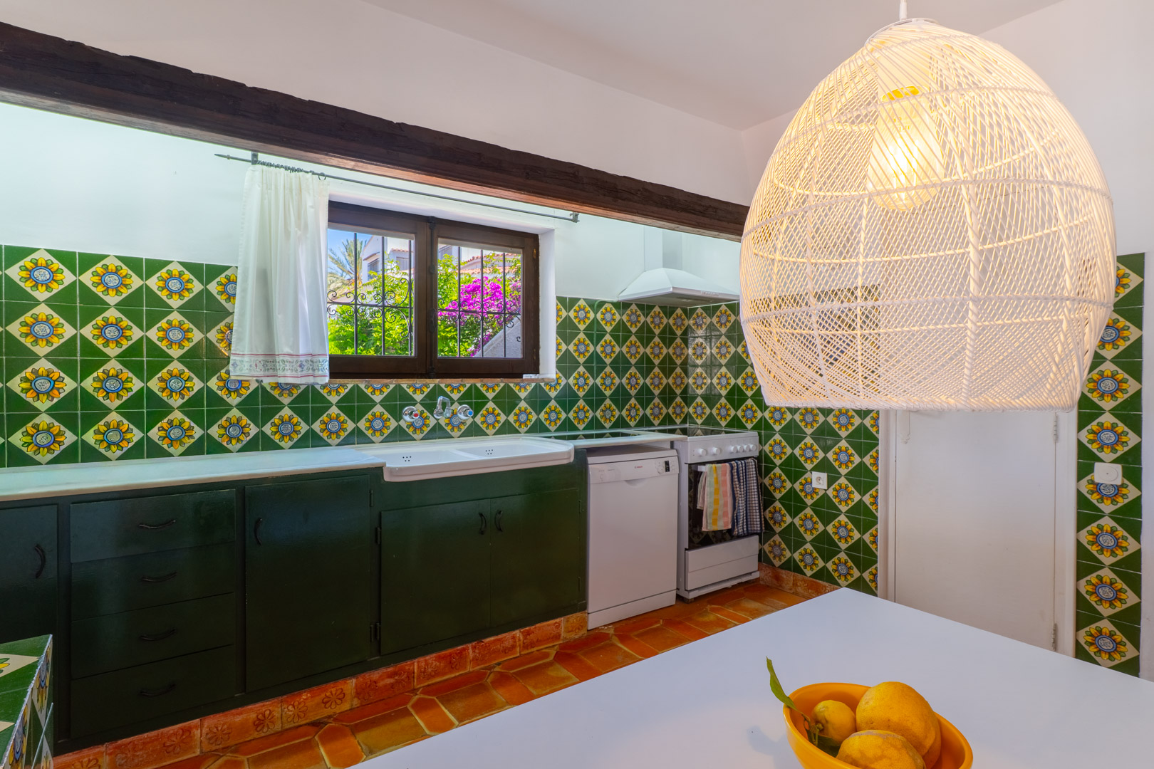 Keuken met decoratieve tegels, donkergroene kasten en een hanglamp van vlechtwerk.