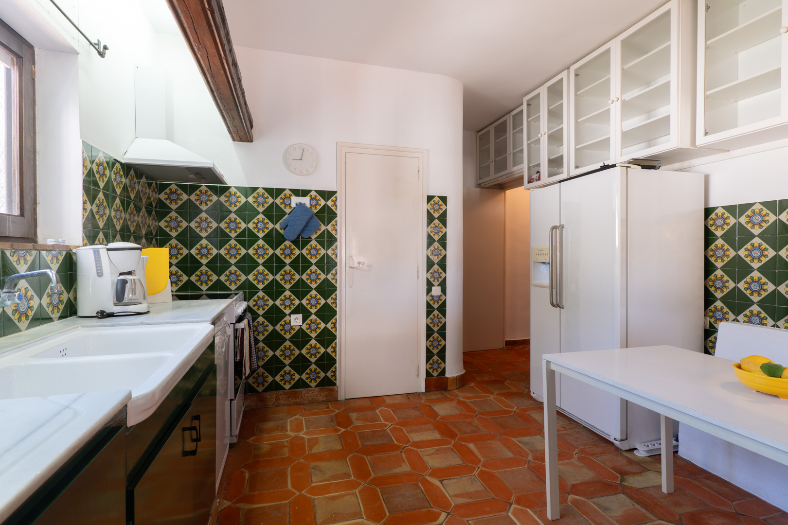Keuken met decoratieve tegels, terracotta vloer en witte bovenkasten.