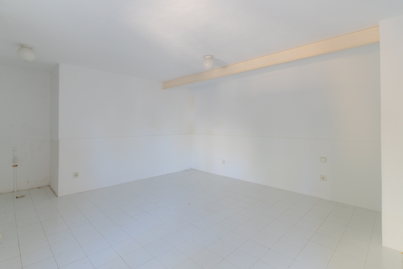 Open ruimte met witte muren, tegelvloer en plafondverlichting.