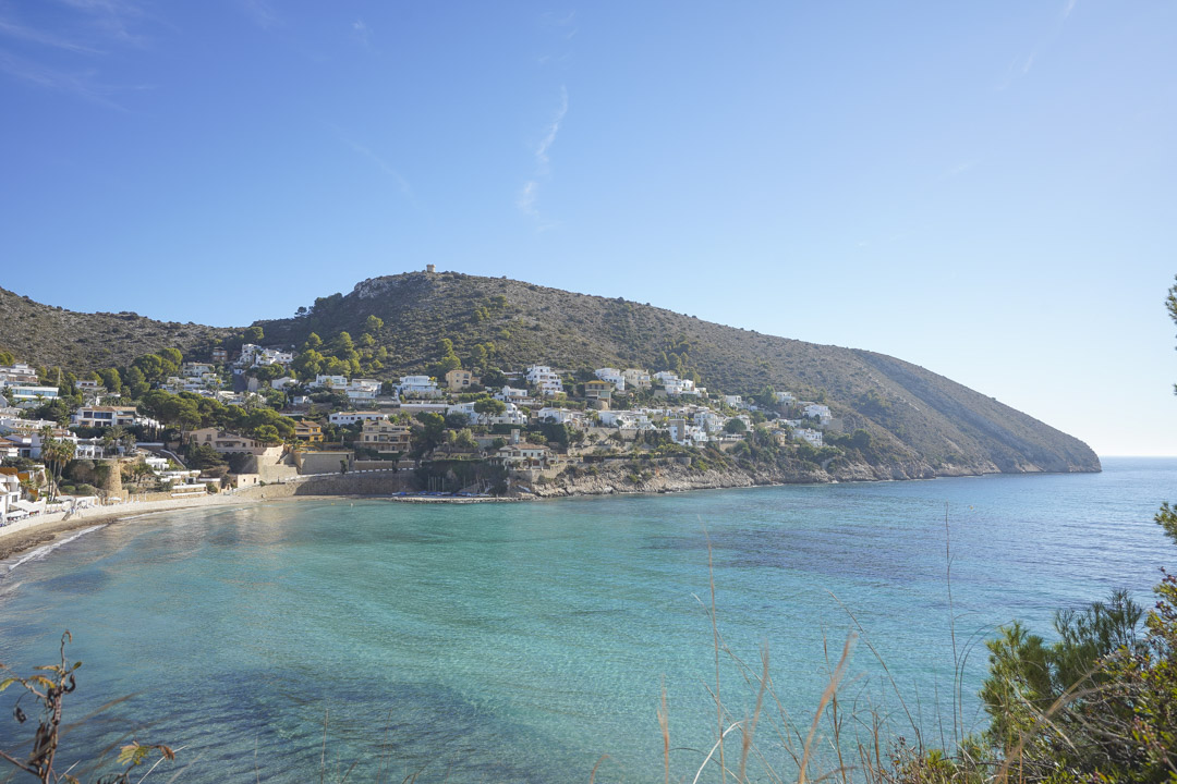 Panoramisch uitzicht op de kustlijn van Moraira met turquoise water en witte huizen op de heuvel.