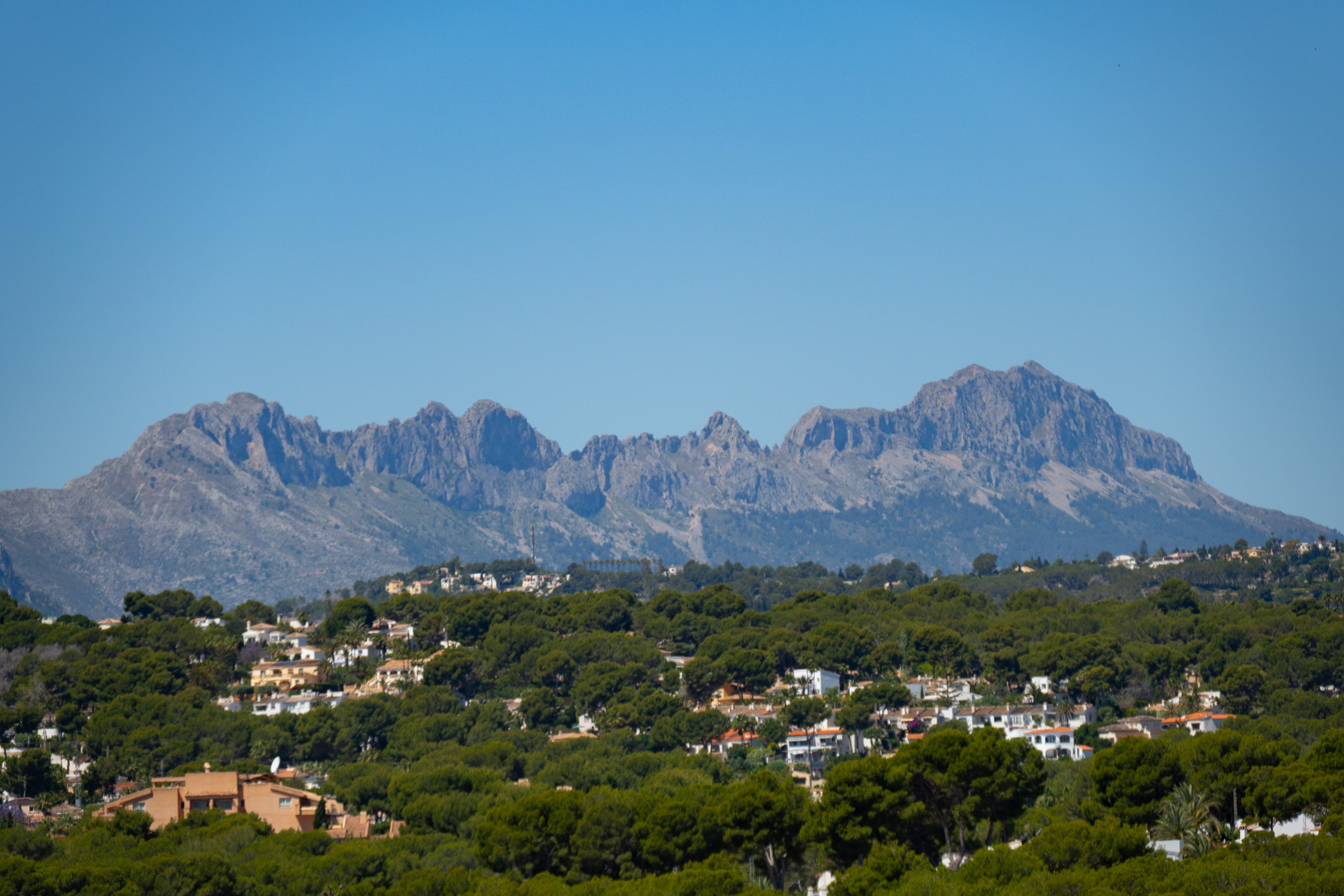 Panoramisch uitzicht op de Sierra de Bernia vanaf de villa, omgeven door groen en andere woningen.