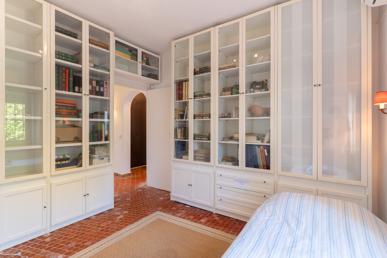 Slaapkamer met ingebouwde witte stellingkasten en terracotta tegelvloer.