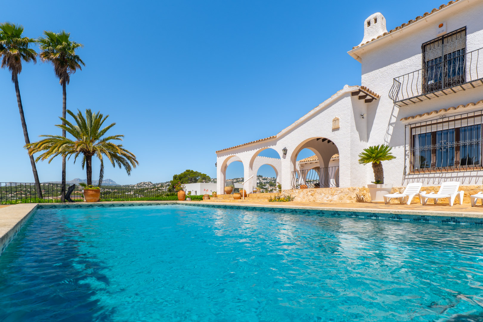 Turkoois zwembad met mozaïekrand en witte villa in mediterrane stijl met bogen.