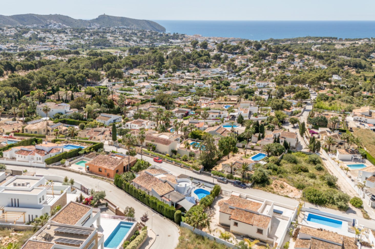Luchtfoto van de woonwijk Moraira, met de dichtheid van villa's met pannendaken, privézwembaden en de blauwe Middellandse Zee aan de horizon.