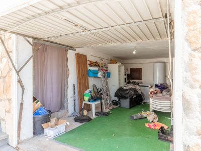 Garage- of opslagruimte met een golfplaten dak en groene kunstgrasvloer. Bevat een boiler, koelkast, ladder en diverse opgeslagen voorwerpen.