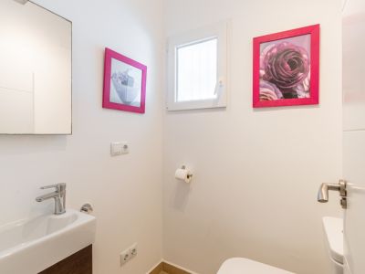 Gastentoilet met rechthoekige wastafel, moderne chromen kraan en donker houtlook meubel. Een klein raam zorgt voor natuurlijk licht, aangevuld met roze ingelijste kunst.