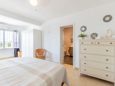 Lichte hoofdslaapkamer met tweepersoonsbed, witte kledingkast en directe toegang tot een en-suite badkamer. Het raam biedt uitzicht op de vegetatie.