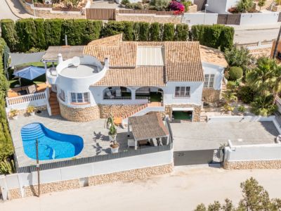 Luchtfoto van de witte villa met terracotta dak en niervormig privézwembad met dolfijnmozaïek. De woning beschikt over een ruime geplaveide oprit en diverse buitenterrassen.