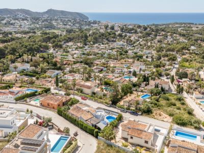 Luchtfoto van de woonwijk Moraira, met de dichtheid van villa's met pannendaken, privézwembaden en de blauwe Middellandse Zee aan de horizon.