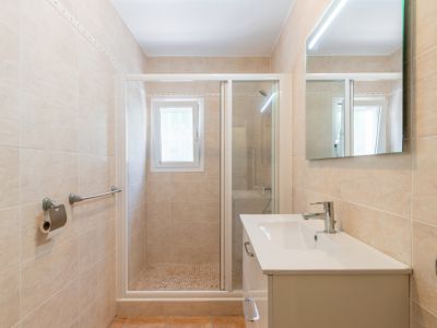 Moderne badkamer met beige wandtegels, een wit badmeubel met chromen kraan, een LED-verlichte spiegel en een inloopdouche met mozaïekvloer en raam.