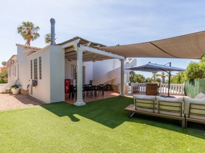 Ruim kunstgras gazon met een moderne buitenbank. Overdekt eetterras met wenteltrap, beschut onder een elegant schaduwdoek.