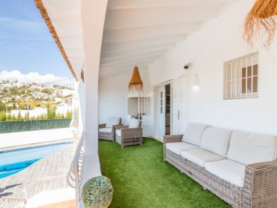 Ruim overdekt terras met comfortabele rieten zitmeubelen op kunstgras, met uitzicht op het privézwembad en de bebouwde heuvels in de verte.